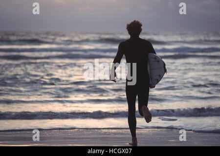 Uomo che porta la tavola da surf a correre verso il mare Foto Stock