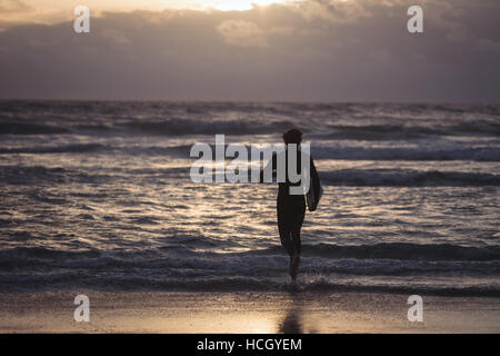 Uomo che porta la tavola da surf a correre verso il mare Foto Stock