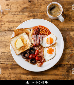 La completa prima colazione Inglese con uova fritte, salsicce, pancetta, fagioli, pane tostato, pomodori e funghi su sfondo di legno Foto Stock