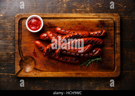 Grigliata di salsicce arrostite e Salsa ketchup sul bordo di taglio su sfondo di legno Foto Stock