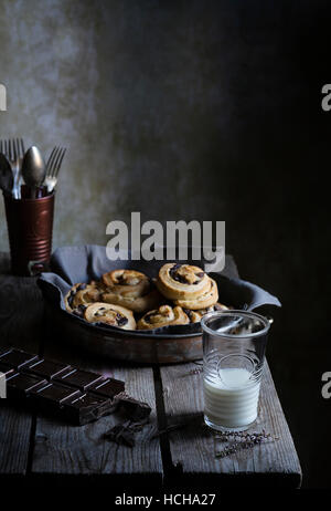 In casa panini alla cannella con un bicchiere di latte sul tavolo rustico Foto Stock