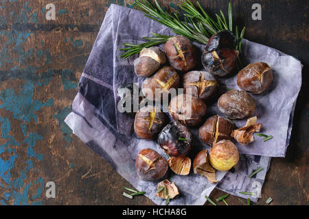 Castagne arrostite nella cenere con rosmarino su carta al di sopra del vecchio dark texture di sfondo di legno. Vista da sopra con spazio per il testo. Foto Stock