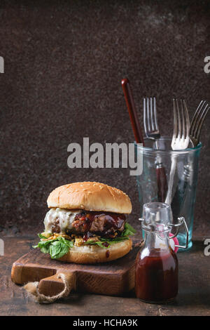 Hamburger di manzo burger cotoletta, cipolla fritti, spinaci, ketchup salsa e formaggio blu nei tradizionali ciambelle, servita su legno tagliere con posate Foto Stock