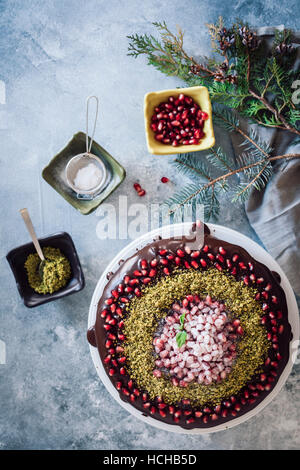 Natale torta di cioccolato decorate con i semi di melograno e pistacchio accompagnato da tre piccole ciotole e pino rami. Foto Stock