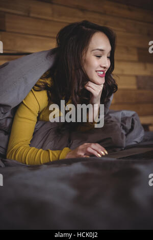 Donna sorridente giacente sul letto tramite computer portatile in camera da letto Foto Stock