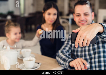 La famiglia, la paternità, tecnologia persone concetto - happy madre, padre e bambina avente la cena tenendo selfie tramite smartphone al ristorante Foto Stock