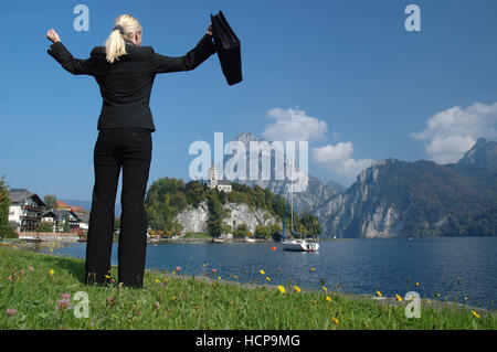 Donna bionda che indossa una tuta in piedi presso il lago Traunsee, celebra il suo successo, Traunkirchen, Austria superiore, Europa Foto Stock