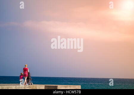 Madre camminando su un molo spingendo la sua PRAM con il suo bambino Foto Stock