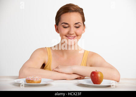 Giovane donna scegliendo tra ciambella e torta per snack Foto Stock