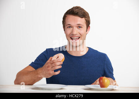 Giovane uomo scegliendo tra ciambella e torta per snack Foto Stock