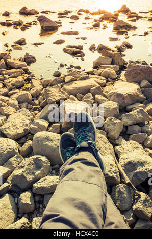 Piedini maschio in tela blu scarpe di sport sul litorale roccioso irregolare di massa. Corsa verticale lifstyle sfondo. Annata calda tonalità foto Foto Stock