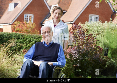 Accompagnatore spingendo Senior uomo in sedia a rotelle Foto Stock