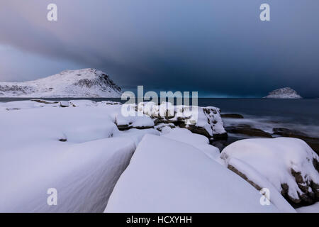 Nuvole temporalesche sulle cime innevate si riflette nel mare freddo di notte, Haukland, Isole Lofoten, nel nord della Norvegia Foto Stock