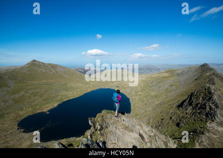 Una donna si erge sulla parte superiore del bordo di estensione con una vista di Red Tarn sotto, Parco Nazionale del Distretto dei Laghi, Cumbria, Regno Unito Foto Stock