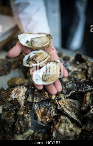 Un uomo può contenere fino a tre aprire le ostriche in un pesce di stallo in London Borough Market, London, Regno Unito Foto Stock