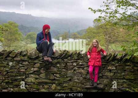 Madre e figlia resto a secco su un muro di pietra mentre è in vacanza nel distretto del lago, Cumbria, Regno Unito Foto Stock