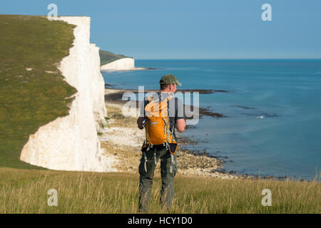 Un uomo si affaccia su chalk scogliere con vedute delle Sette sorelle del litorale, South Downs National Park, East Sussex, Regno Unito Foto Stock