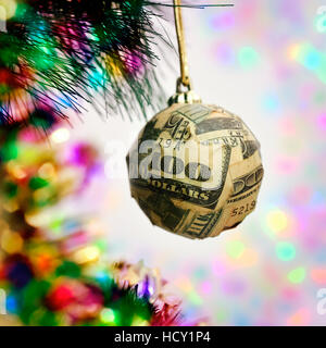 Una palla di Natale avvolti in pezzi di un centinaio di dollar banconota appeso al ramo di un albero di natale Foto Stock
