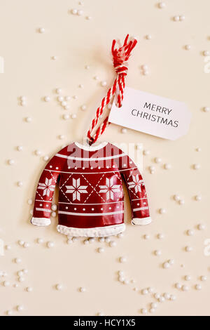 Alta angolazione di un ornamento di Natale con una etichetta di carta ad essa legate con il testo buon natale, collocata su una superficie bianca spruzzata con sma Foto Stock