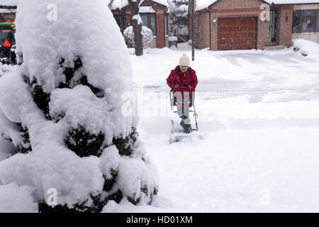 Donna che utilizza eco-friendly Snow Plough aratura è la sua strada in inverno con un sacco di neve fresca in Ontario, Canada Foto Stock