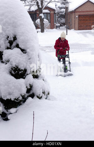 Donna che utilizza eco-friendly Snow Plough aratura è la sua strada in inverno con un sacco di neve fresca in Ontario, Canada Foto Stock