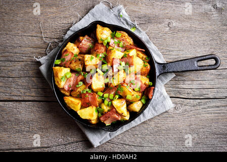 Patate fritte con pancetta e cipolla verde su sfondo di legno, vista dall'alto Foto Stock