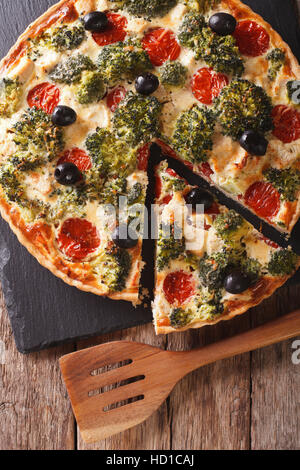 Torta salata con pollo, broccoli, pomodoro e olive vicino sul tavolo. vista verticale da sopra Foto Stock