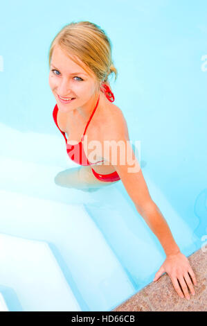 Giovane, attraente donna che indossa un bikini rosso in un pool Foto Stock