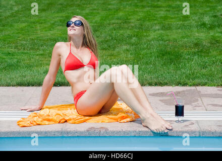 Giovane, attraente donna che indossa un bikini rosso e prendere il sole vicino alla piscina Foto Stock