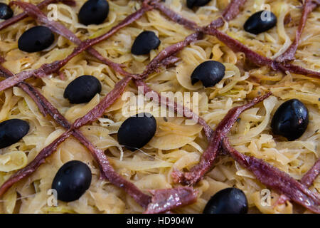 Reticolo di acciughe e olive su cuocere le cipolle sulla pasta sfoglia quando rendendo pissaladiere, pronto per la cottura da vicino. Foto Stock