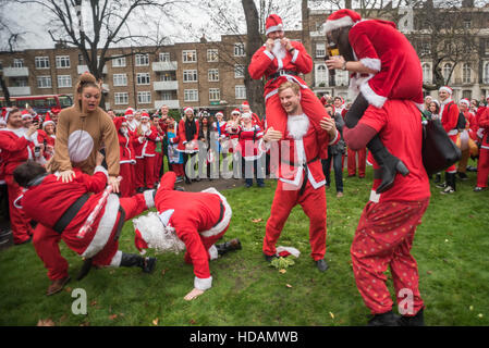 Londra, Regno Unito. Il 10 dicembre 2016. La North London Santacon in pausa nel parco al Mornington Crescent e alcuni hanno preso parte ad alcune giostre informale. Molti sacchetti trasportati con le lattine di birra o di bottiglie di vino che hanno bevuto sul percorso e si ferma dove hanno cantato e ballato e jousted, con l'occasionale germoglio di Bruxelles lotta tra babbo natale e gli elfi. Credito: Peter Marshall / Alamy Live News Foto Stock