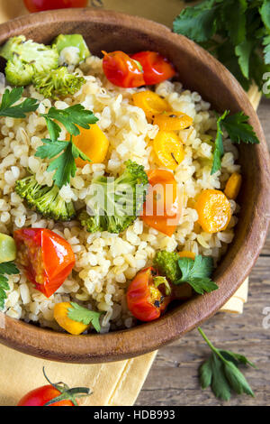 Deliziosa casa di bulgur vegetariano (cuscus) con verdure: pomodori, carote, zucchine, broccoli e prezzemolo in legno rustico bowl - veg sani Foto Stock