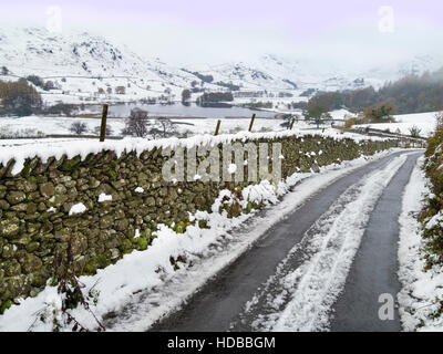 Vicolo innevato con muro di pietra a secco a Little Langdale con tarn Beyond, English Lake District, Cumbria, Inghilterra, Regno Unito. Foto Stock