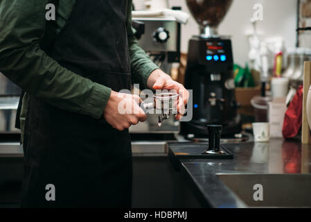 Le mani dell'uomo in grembiule nero che predispone la macchina per il caffè Foto Stock