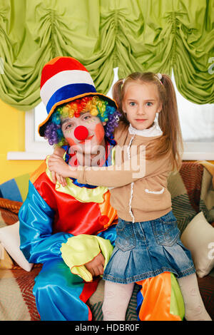 Bambina abbracciando un allegro clown. Foto Stock