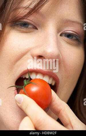 Donna di mordere in un pomodoro ciliegino Foto Stock