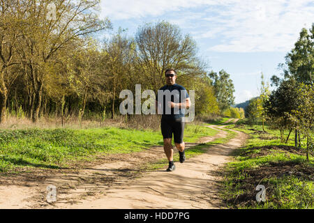 Grande pancia uomo jogging , esercitare, facendo cardio nel parco , leggermente sovrappeso, perdere peso. In un prato di erba verde tra alberi senza lea Foto Stock