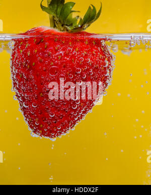 Fragola in acqua frizzante contro uno sfondo giallo Foto Stock