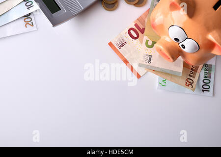 Concetto di risparmio e di contabilità con salvadanaio ed impilate le monete e le bollette e calcolatrice sul tavolo e sfondo bianco. Composizione orizzontale. Parte superiore Foto Stock