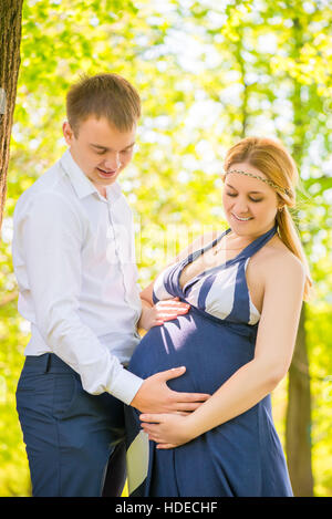 Caring papà strofinarsi il ventre di una moglie incinta nel parco Foto Stock