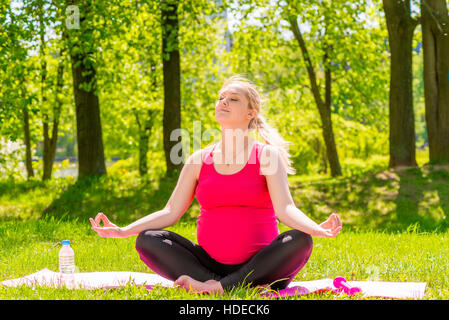 Felice donna incinta in una posizione del loto facendo yoga nel parco Foto Stock