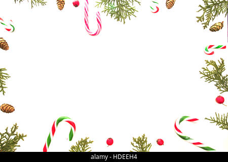 Composizione di natale su sfondo bianco. Xmas frame con candy canes, verde thuja ramoscelli, pigne e red rose selvatiche frutti. Vista superiore, piatto laici. Foto Stock