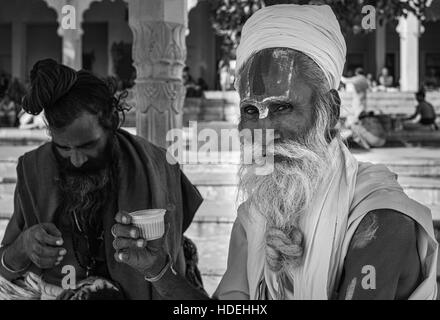 Un sadhu, Indù santo uomo, vestito in abito tradizionale gode di una pausa e la tazza di tè durante il pellegrinaggio alla città santa di Pushkar Foto Stock