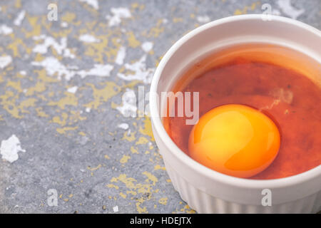 Materie uova con pomodori in ramekins sul tavolo di pietra Foto Stock