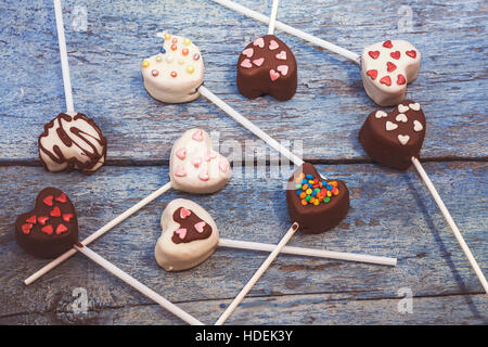 Molti POP di torta a forma di cuore giacciono sul vecchio blu sullo sfondo di legno vista dall'alto. Foto Stock