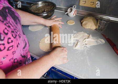 Nonna stendere l'impasto. Senior donna mani di stendere la pasta di farina con il mattarello nella sua cucina domestica. Foto Stock