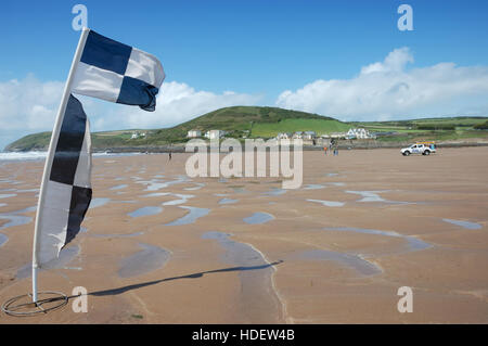 In bianco e nero a scacchi spiaggia RNLI sicurezza battenti bandiera su Croyde Bay Beach con un bagnino RNLI veicolo nella distanza. Foto Stock