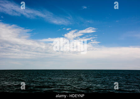 Modellato nuvole bianche in un cielo blu su un increspato azzurro mare. Foto Stock