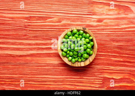 Fresco verde pisello nella ciotola sul rosso sfondo di legno Foto Stock