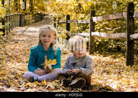 Fratello e Sorella e fratelli germani seduti su foglie di autunno nel parco Foto Stock